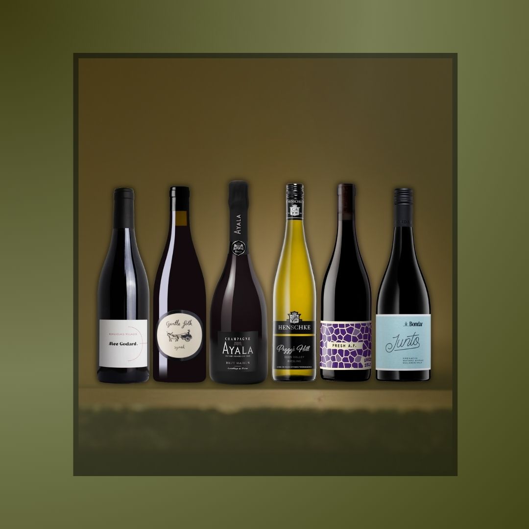 A framed vertical artwork showing six wine bottles lined up against a warm brown gradient background, set on an olive green backdrop. The bottles include dark red, white, black, yellow, and purple labels.