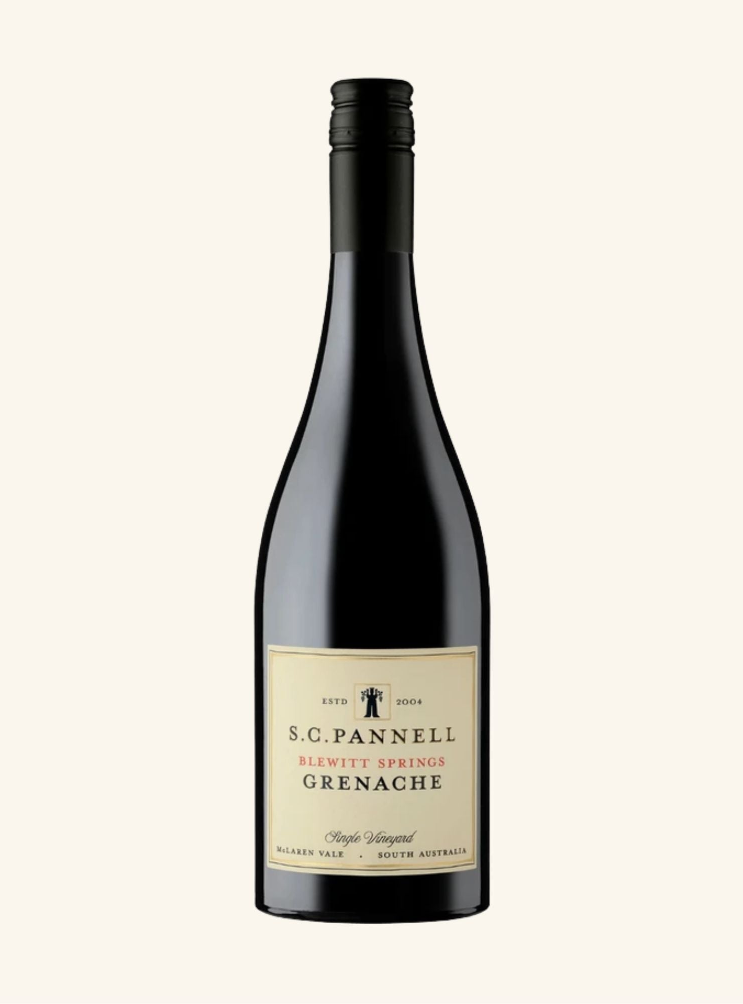 A dark coloured wine bottle with a pale yellow label with black and red writing, on an off white background.