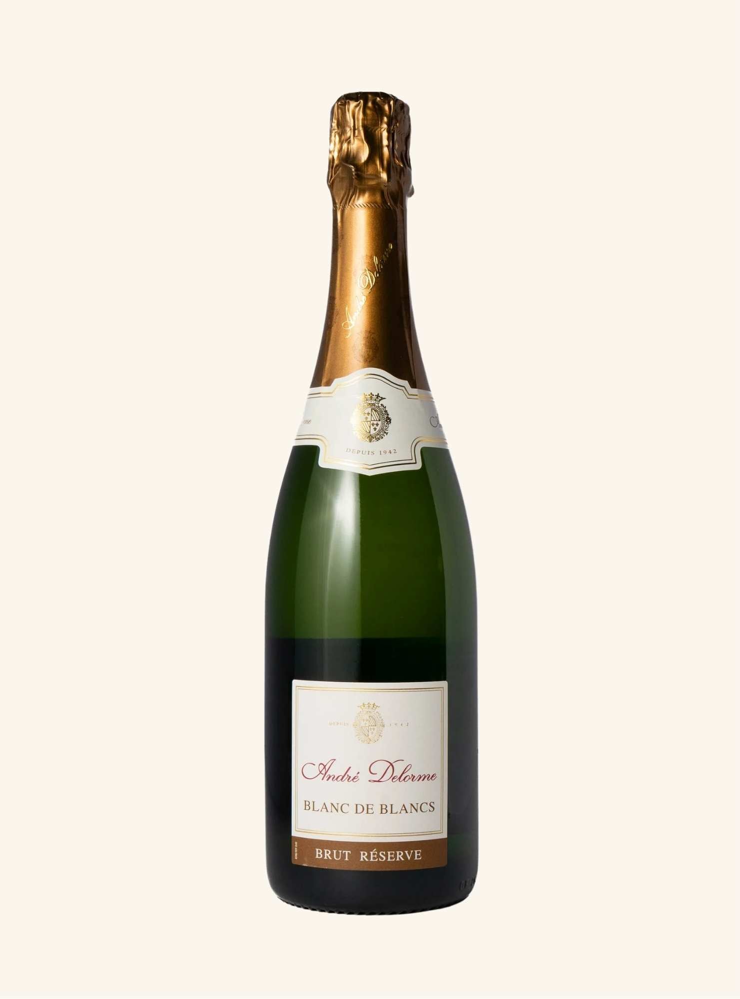 A bottle of Andre Delorme Blanc de Blancs Brut Réserve sparkling, featuring a dark green glass bottle, gold foil neck, and cream-colored labels, set against a solid off-white background.